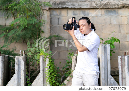 Professional Asian Chinese - Thai Camera man posture and focus in viewfinder and LED screen on mirrorless camera medium format in construction concrete area. Professional Asian Chinese - Thai Camera man posture and focus in viewfinder and LED screen on mirrorless camera medium format in construction concrete area. 97878079