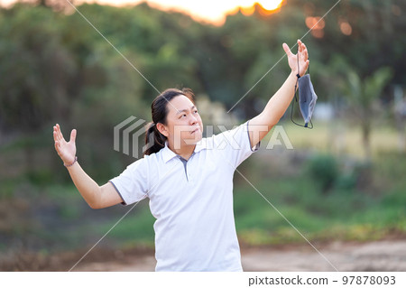 Asian Man take off mask and rise his hand up in golden twilight time. Asian Man take off mask and rise his hand up in golden twilight time. 97878093