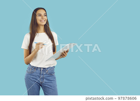 Happy woman standing on blue copy space background, holding clipboard, looking away and smiling 97878606