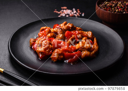 Delicious juicy meat with hot peppers and sauce on a black ceramic plate 97879858