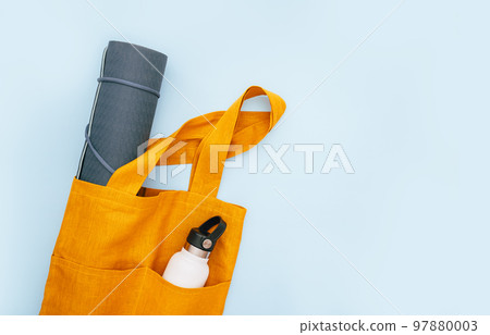 Rolled blue yoga mat. Yoga block with water bottle in orange tote bag. Weight loss. fitness and exercise concept. Active lifestyle sport. Workout at home or gym app Rolled blue yoga mat. Yoga block with water bottle in orange tote bag. Weight loss. fitness and exercise concept. Active lifestyle sport. Workout at home or gym app 97880003