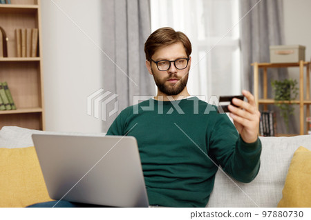 Serious Man Holding Credit Card. Bearded Man Paying Online, Using Laptop 97880730