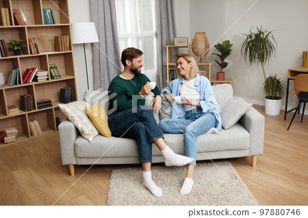 Happy Couple Drinking Coffee At Home. Young Couple Talking And Holding Cups Happy Couple Drinking Coffee At Home. Young Couple Talking And Holding Cups 97880746