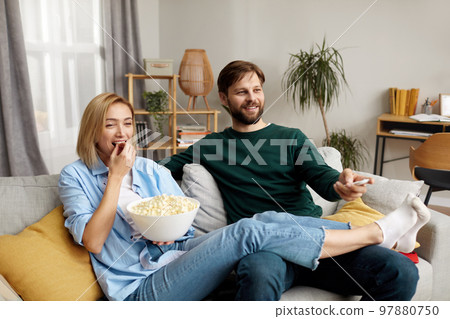 Laughing Couple Watching TV At Home. Loving People Resting On Sofa 97880750