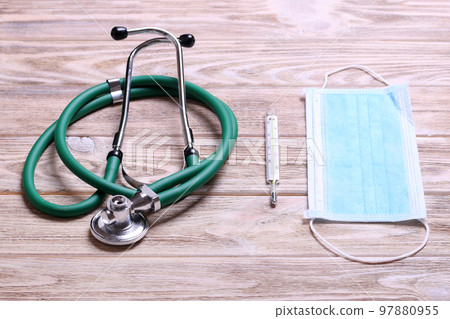 Top view of stethoscope, protective mask and mercury thermometer on yellow wooden background. Medical instruments concept Top view of stethoscope, protective mask and mercury thermometer on yellow wooden background. Medical instruments concept 97880955