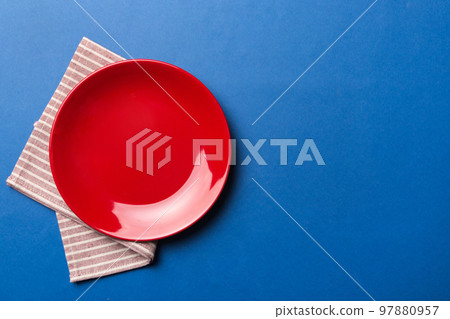 Top view on colored background empty round red plate on tablecloth for food. Empty dish on napkin with space for your design Top view on colored background empty round red plate on tablecloth for food. Empty dish on napkin with space for your design 97880957