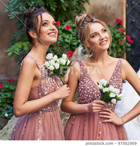 Beautiful bridesmaids in gorgeous elegant stylish red pink violet floor length v neck chiffon gown dress decorated with sequins sparkles and rhinestones holding flowers bouquets. Wedding day in old 97882909