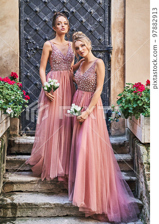 Beautiful bridesmaids in gorgeous elegant stylish red pink violet floor length v neck chiffon gown dress decorated with sequins sparkles and rhinestones holding flowers bouquets. Wedding day in old Beautiful bridesmaids in gorgeous elegant stylish red pink violet floor length v neck chiffon gown dress decorated with sequins sparkles and rhinestones holding flowers bouquets. Wedding day in old 97882913