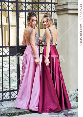 Two beautiful bridesmaids girls blonde and brunette ladies wearing elegant full length purple violet lilac lavender satin folded bridesmaid dress with silver sequined camisole top with sequins 97882933