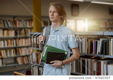 Smart male student chooses book while standing in the university library Smart male student chooses book while standing in the university library 97883307
