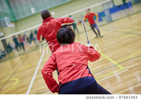 Back view of a woman playing badminton in a gym in winter 97883363
