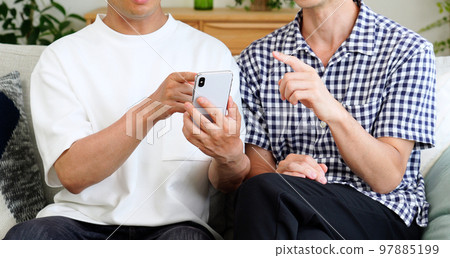 A male couple having a conversation looking at a smartphone at home A male couple having a conversation looking at a smartphone at home 97885199