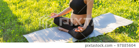 Banner pregnant woman is meditating while sitting on yoga mat on lawn sunny summer evening copy space. Concept of pacification and energy boost. Banner pregnant woman is meditating while sitting on yoga mat on lawn sunny summer evening copy space. Concept of pacification and energy boost. 97885604