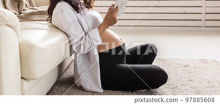 Banner pregnant woman holding digital while tablet sitting on carpet near couch in living room home copy space Banner pregnant woman holding digital while tablet sitting on carpet near couch in living room home copy space 97885608