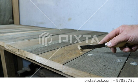 filling up holes and cracks on a wooden surface with a narrow trowel in a man's hand, patching up irregularities on a structure made of rough boards in a workshop or garage close-up 97885785