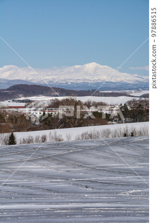 Fields and snowy mountains covered with snow-melting agent on a sunny winter day Daisetsuzan 97886515