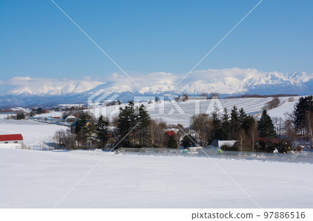 Fields and snowy mountains covered with snow-melting agent on a sunny winter day Tokachidake mountain range 97886516