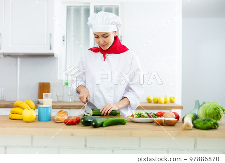 Proffesional woman cook in white uniform chopping vegetables Proffesional woman cook in white uniform chopping vegetables 97886870