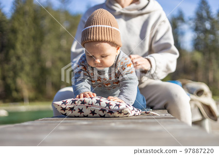 Happy family. Young mother playing with her baby boy infant oudoors on sunny autumn day. Portrait of mom and little son on wooden platform by lake. Positive human emotions, feelings, joy Happy family. Young mother playing with her baby boy infant oudoors on sunny autumn day. Portrait of mom and little son on wooden platform by lake. Positive human emotions, feelings, joy 97887220