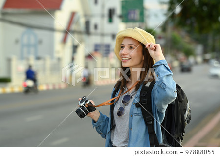 Young female tourist with backpack and digital camera standing on city street. Blogger, vacation and journey concept Young female tourist with backpack and digital camera standing on city street. Blogger, vacation and journey concept 97888055
