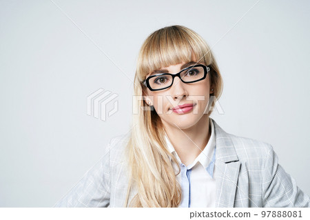 Closeup portrait of happy young beautiful blonde woman in studio on light gray background. Smiling model in pantsuit and glasses. 97888081