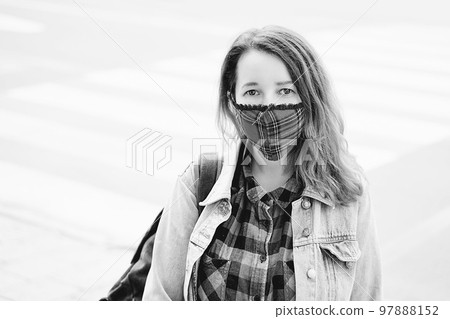 Young woman wearing a plaid handmade face mask and colorful shirt standing on the street. 97888152