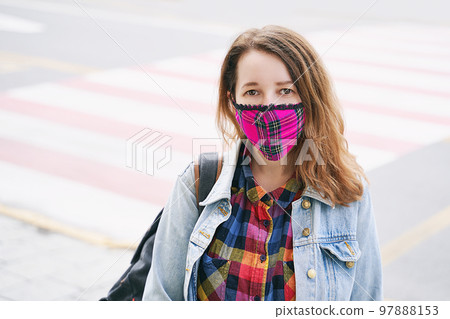 Young woman wearing a plaid handmade face mask and colorful shirt standing on the street. 97888153