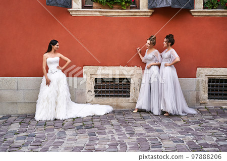 Beautiful bride and bridesmaids in gorgeous elegant stylish light grey silver floor length dresses in old beautiful European city having fun on a wedding day. 97888206