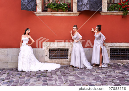 Beautiful bride and bridesmaids in gorgeous elegant stylish light grey silver floor length dresses in old beautiful European city having fun on a wedding day. Beautiful bride and bridesmaids in gorgeous elegant stylish light grey silver floor length dresses in old beautiful European city having fun on a wedding day. 97888258