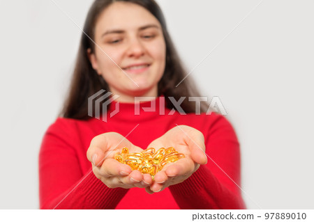 A woman smiling holds in her palms a handful of capsules of fish oil, omega 3. A woman smiling holds in her palms a handful of capsules of fish oil, omega 3. 97889010