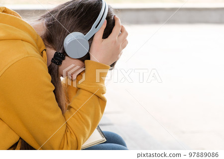 Sad teenage girl in headphones will cover her face with her hands, a place for text Sad teenage girl in headphones will cover her face with her hands, a place for text 97889086
