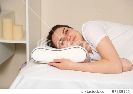 A woman lies on an orthopedic pillow, looks into the camera and smiles. A woman lies on an orthopedic pillow, looks into the camera and smiles. 97889165