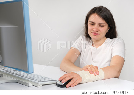 A woman with an elastic bandage on her wrist sits in front of a computer, carpal tunnel syndrome A woman with an elastic bandage on her wrist sits in front of a computer, carpal tunnel syndrome 97889183