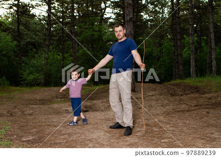 Dad and son walk in the coniferous pine forest in the evening and play with sticks. Father's Day, the role of dad in the child's life. 97889239