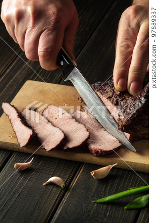 Slicing baked beef meat before preparing dinner with the chef's hands. Top view cooking process concept. Peasant foods. Slicing baked beef meat before preparing dinner with the chef's hands. Top view cooking process concept. Peasant foods. 97889337