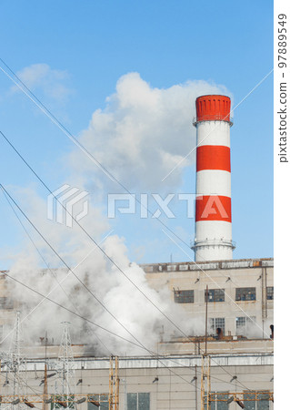 Pollution of the environment, ecology and air. Withdrawal of combustion products of soot, smoke and gases from the pipe of an industrial plant into the atmosphere against the background of a blue sky 97889549