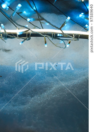 Blue icy snow is illuminated with festive LED garlands vertical photo, New Year card template with copy space for text or image. Winter holidays, Christmas, Hanukkah light blue background or backdrop. 97889640