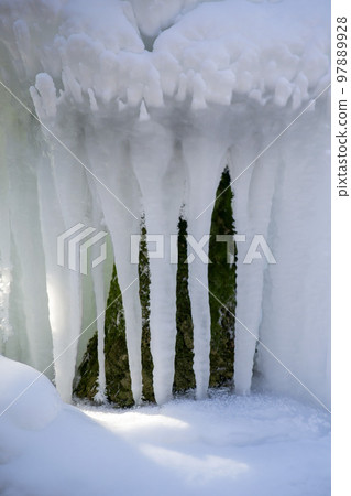 Iced fountain in the park on a winter sunny day. Fountain with frozen water. A jet of water from a fountain that iced over in the cold. Background covered with ice and snow in the park on day Iced fountain in the park on a winter sunny day. Fountain with frozen water. A jet of water from a fountain that iced over in the cold. Background covered with ice and snow in the park on day 97889928