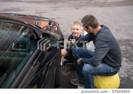 Cute boy helps Dad fix the car. Unscrew the wheel 97889969