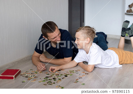 A cute boy with a cheerful dad is collecting a puzzle lying on the floor in a room 97890115