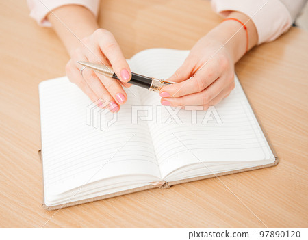 Close up of a woman's hands writing in a notepad placed on a wooden table, home office and work concept, plans and thoughts Close up of a woman's hands writing in a notepad placed on a wooden table, home office and work concept, plans and thoughts 97890120