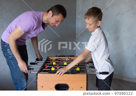 Cute boy playing table football with his emotional dad in the room Cute boy playing table football with his emotional dad in the room 97890122