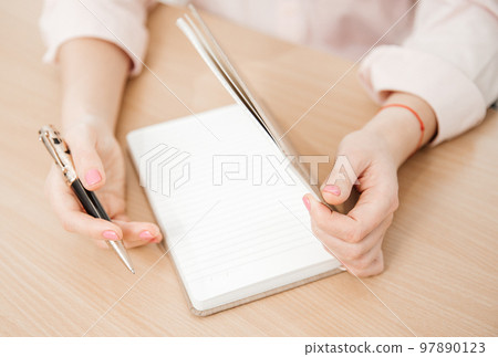 Close up of a woman's hands writing in a notepad placed on a wooden table, home office and work concept, plans and thoughts Close up of a woman's hands writing in a notepad placed on a wooden table, home office and work concept, plans and thoughts 97890123