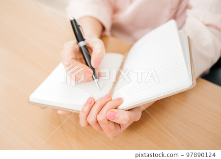 Close up of a woman's hands writing in a notepad placed on a wooden table, home office and work concept, plans and thoughts Close up of a woman's hands writing in a notepad placed on a wooden table, home office and work concept, plans and thoughts 97890124