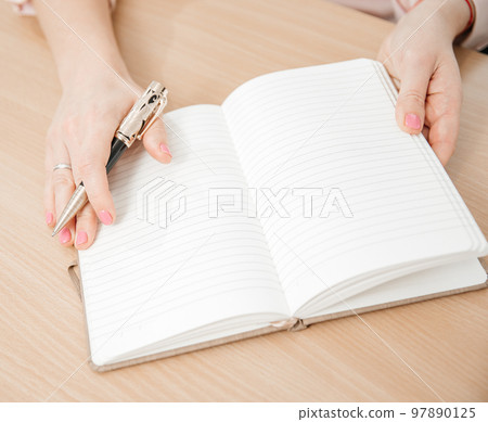Close up of a woman's hands writing in a notepad placed on a wooden table, home office and work concept, plans and forecasts Close up of a woman's hands writing in a notepad placed on a wooden table, home office and work concept, plans and forecasts 97890125