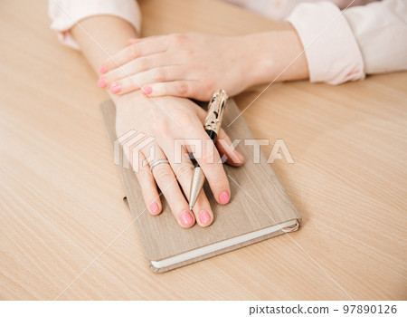 Close up of a woman's hands writing in a notepad placed on a wooden table, home office and work concept, plans and business meeting Close up of a woman's hands writing in a notepad placed on a wooden table, home office and work concept, plans and business meeting 97890126