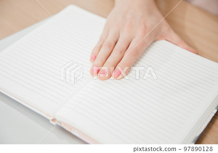 Close up of a woman's hand writing in a notepad placed on a wooden table, home office and work concept, plans and forecasts Close up of a woman's hand writing in a notepad placed on a wooden table, home office and work concept, plans and forecasts 97890128