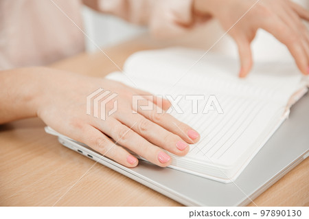 Close up of a woman's hands writing in a notepad placed on a wooden table, home office and work concept, plans and business meeting Close up of a woman's hands writing in a notepad placed on a wooden table, home office and work concept, plans and business meeting 97890130
