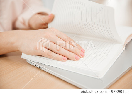 Close up of a woman's hands writing in a notepad placed on a wooden table, home office and work concept, plans and forecasts Close up of a woman's hands writing in a notepad placed on a wooden table, home office and work concept, plans and forecasts 97890131