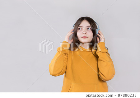 A teenage girl in a bright hooded sweatshirt on her head and headphones looks at the space for the text to the side. Learning online, schooling remotely. On a light background. A teenage girl in a bright hooded sweatshirt on her head and headphones looks at the space for the text to the side. Learning online, schooling remotely. On a light background. 97890235